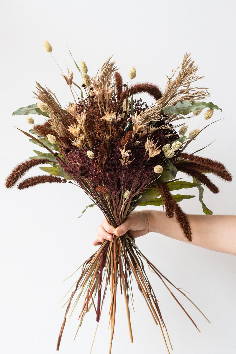 Hand holding "Allspice" autumnal floral preserved arrangement by Sprout Home in front of white background