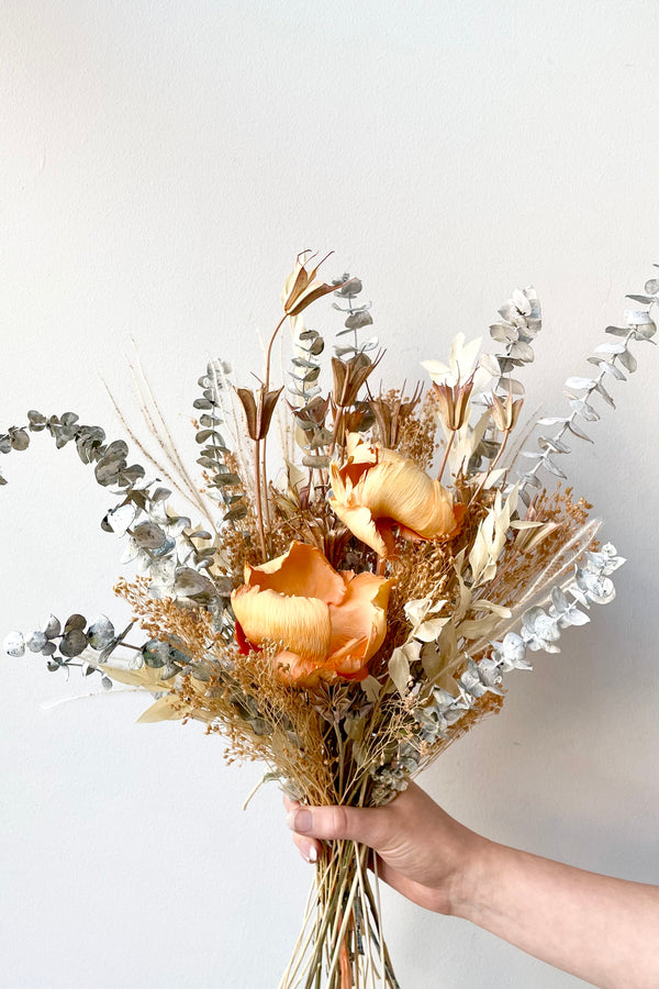 A hand holds the $60 version of Preserved Arrangement Creamsicle by Sprout Home against a white backdrop