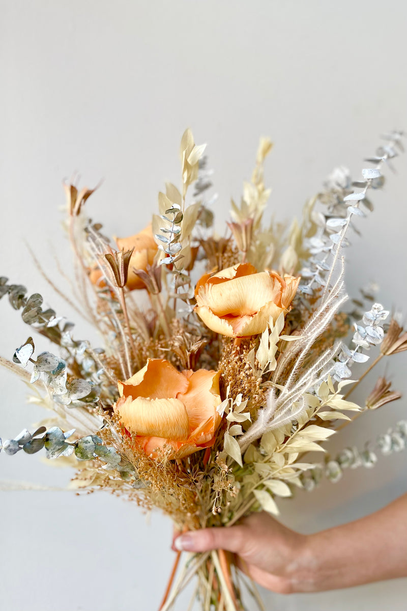 A hand holds the $85 option of Preserved Arrangement Creamsicle by Sprout Home against a white backdrop