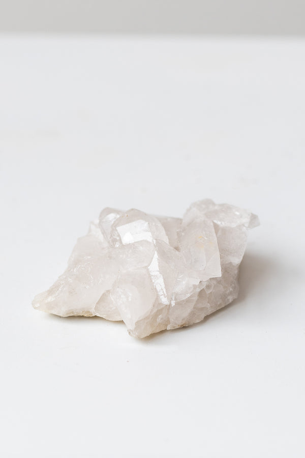 Clear quartz cluster on white surface in front of grey background