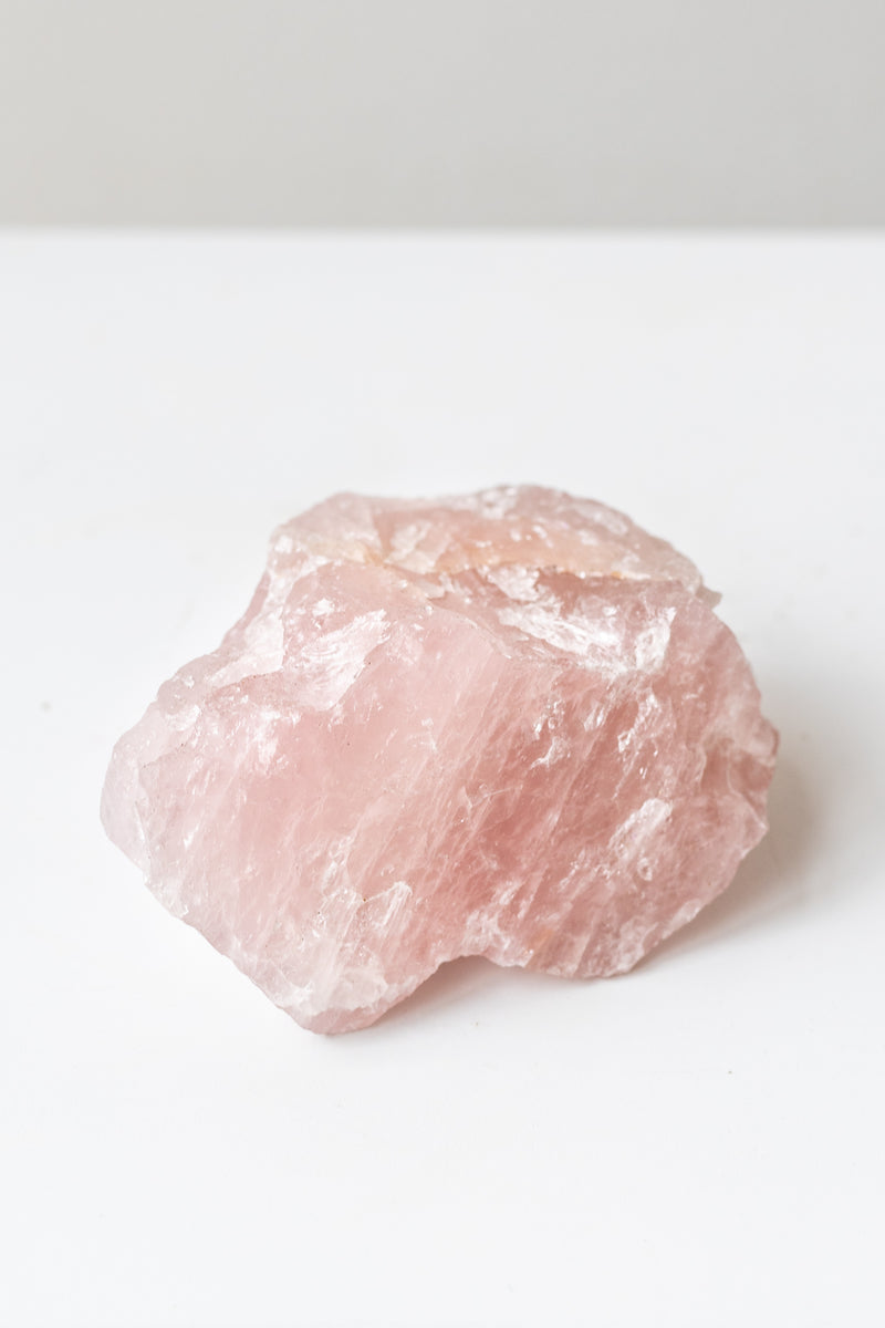 Rose quartz crystal on white surface in front of grey background