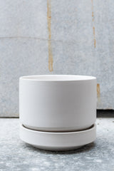 White stoneware planter with matching saucer by LBE Designs sits in front of a grey background