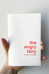 A hand holds The Angry Fairy - Book to Illustrate  against a white backdrop.