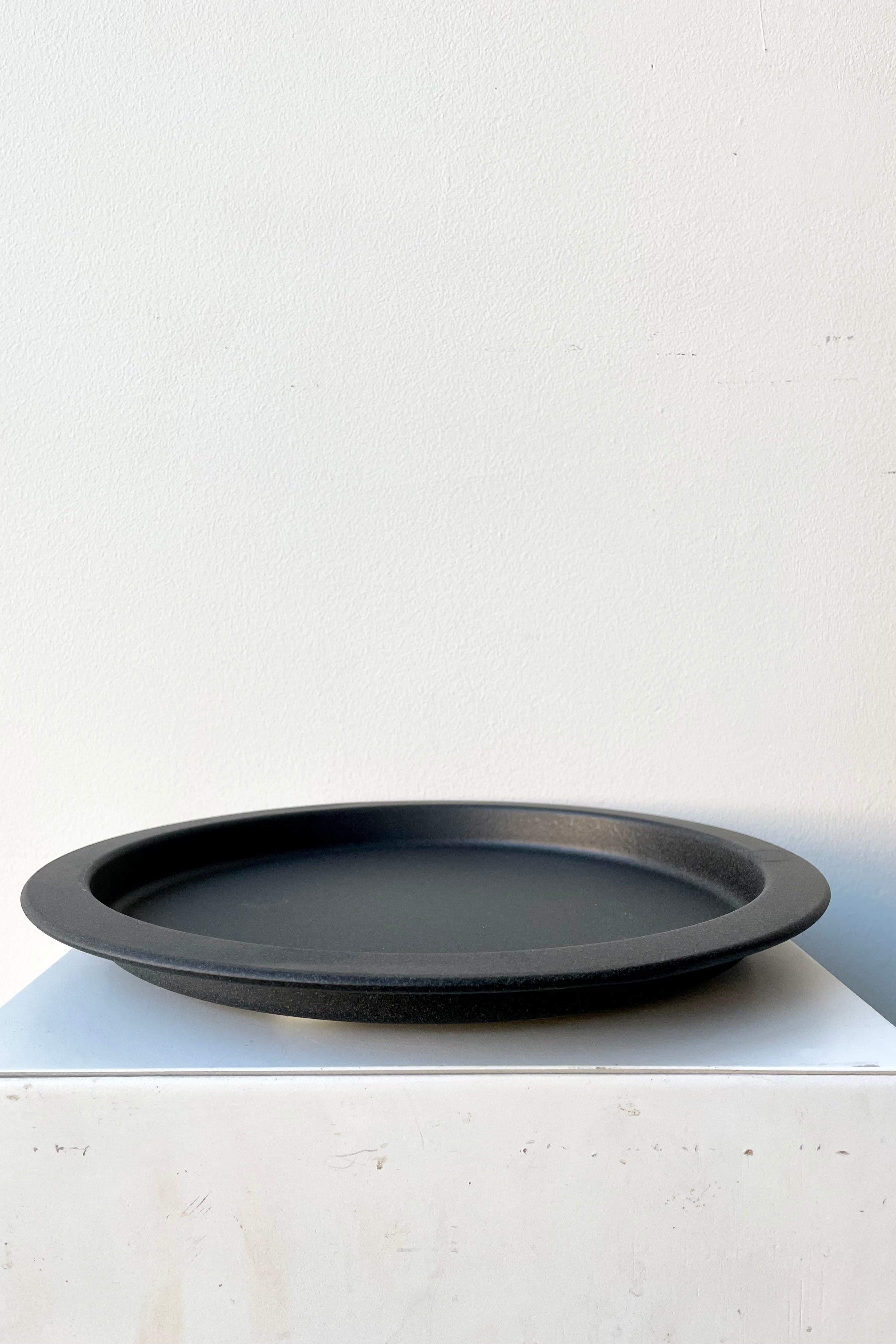 A speckled grey saucer against a while wall at Sprout Home. 