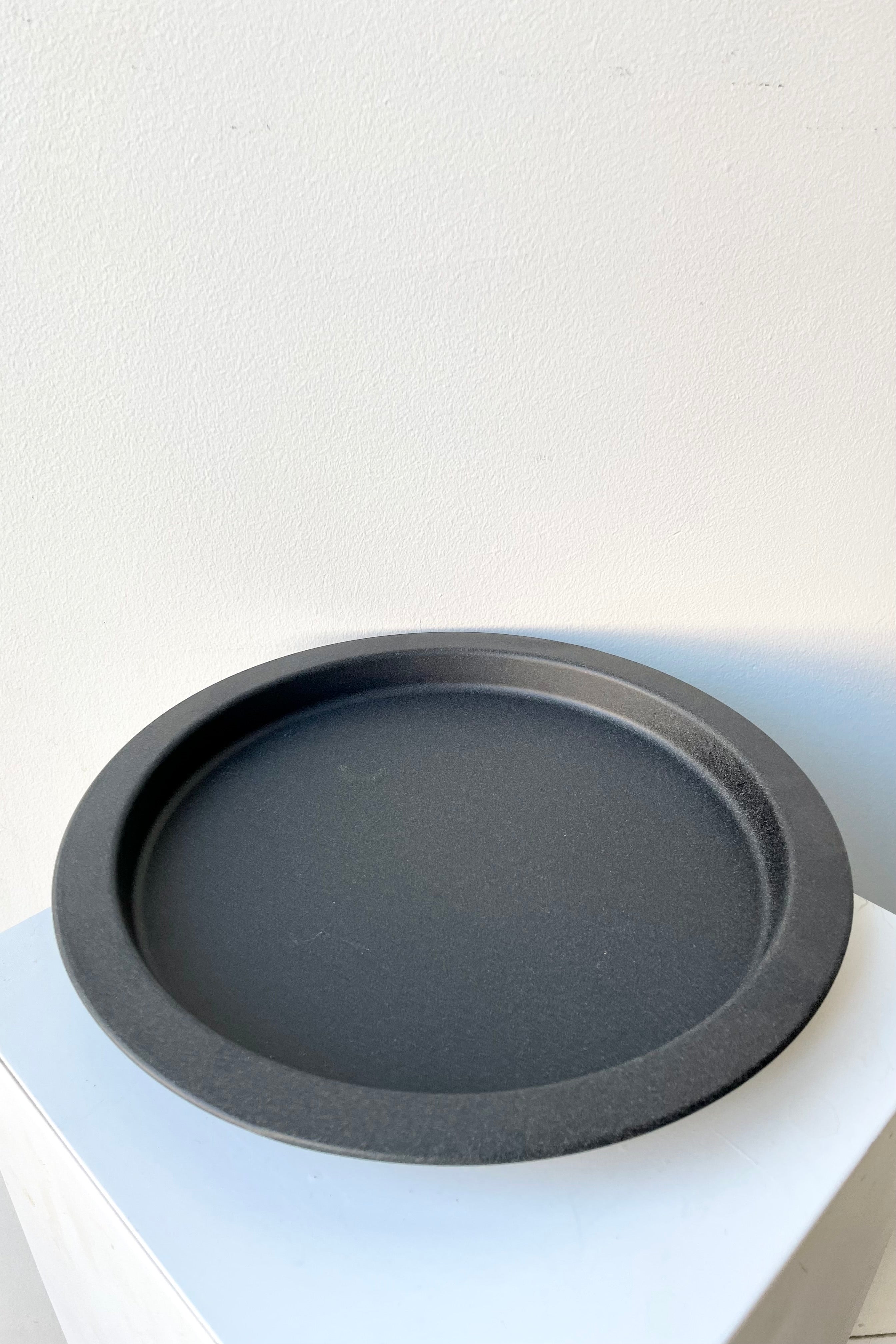 A speckled grey saucer against a while wall at Sprout Home. 