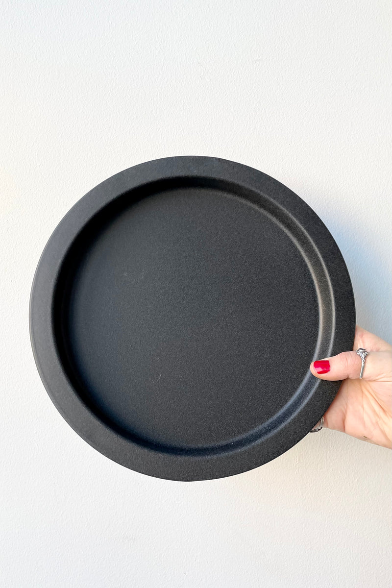 A speckled grey saucer held against a while wall at Sprout Home. 