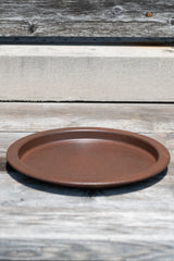 10" textured copper metal plant saucer on a grey wood surface