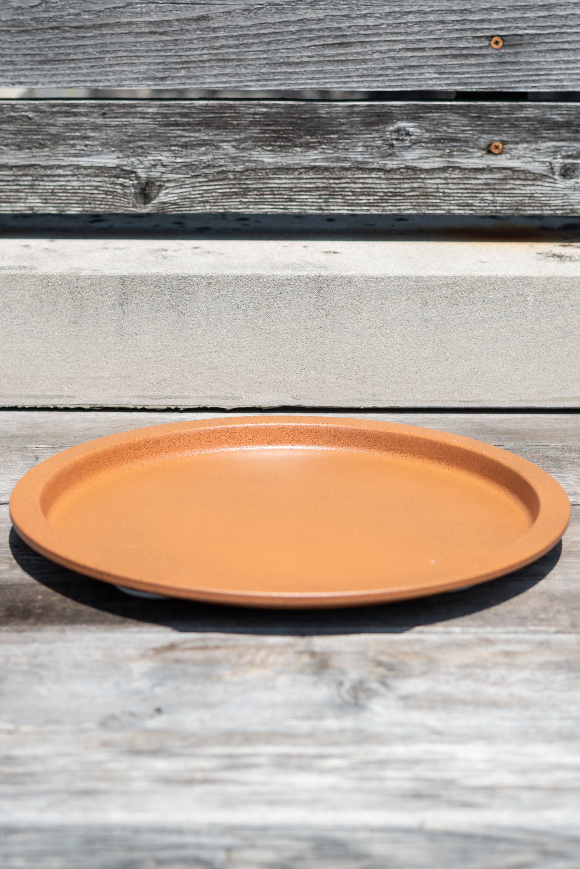 13" clay metal plant saucer on a grey wood surface