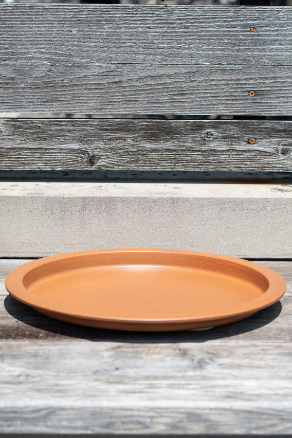 15" clay metal plant saucer on a grey wood surface