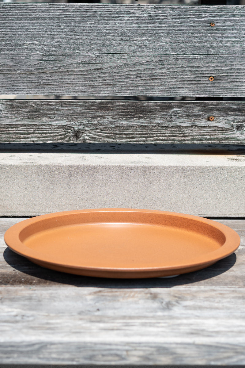 15" clay metal plant saucer on a grey wood surface