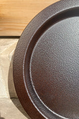 A detailed view of the 15" Saucer in textured copper against a wood backdrop