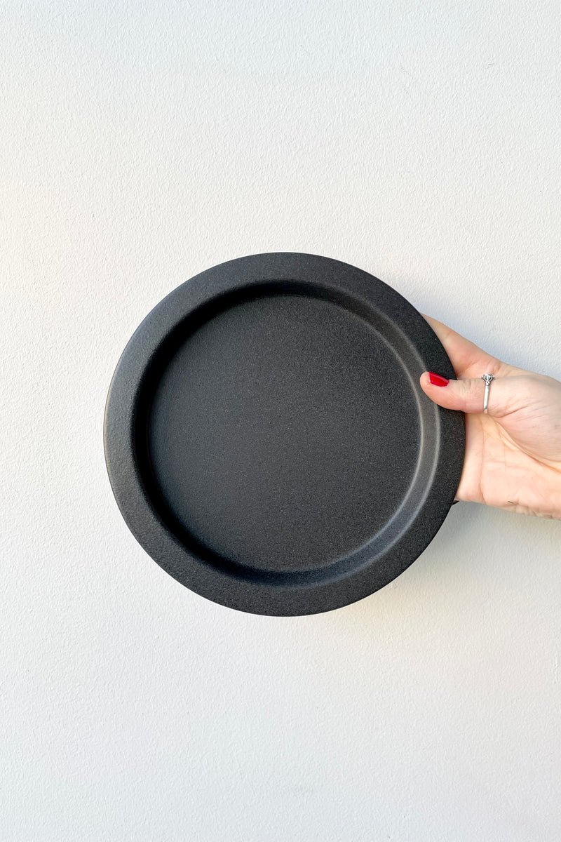 8" speckled grey saucer being held up against a white wall at Sprout Home. 