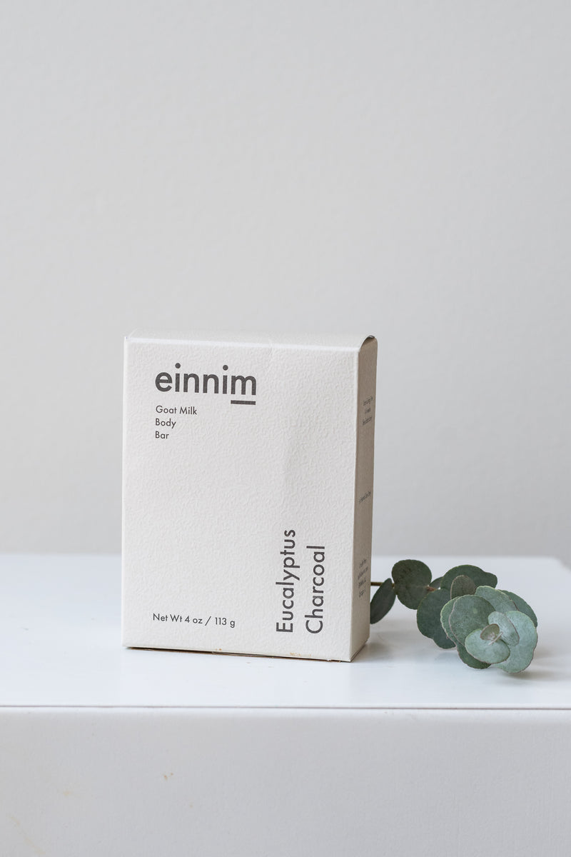 Eucalyptus Charcoal body bar soap by EINNIM with sprig of eucalyptus in front of white background