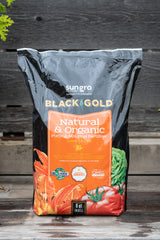 Black Gold Natural and Organic potting mix plus fertilizer bag in front of grey wood background