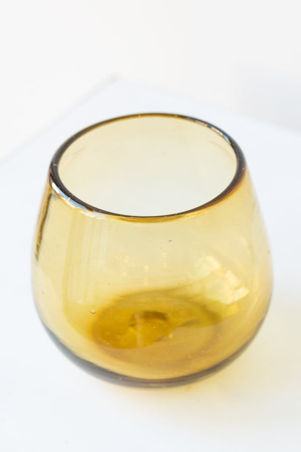 Stemless amber colored wine glass on a white surface in a white room