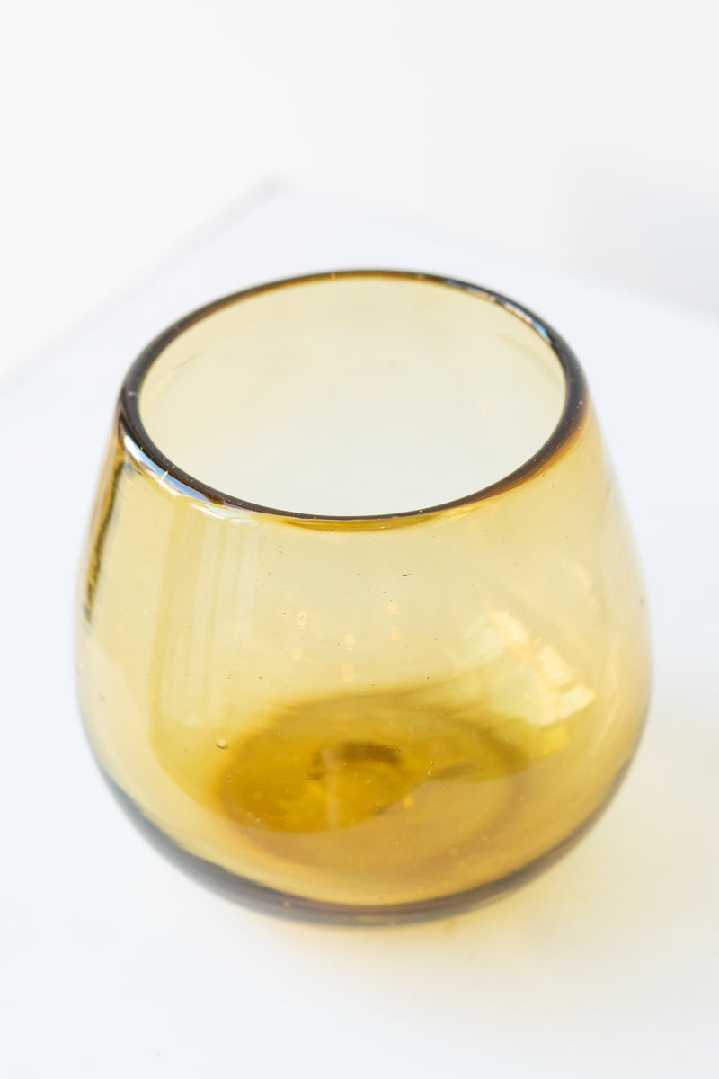 Stemless amber colored wine glass on a white surface in a white room