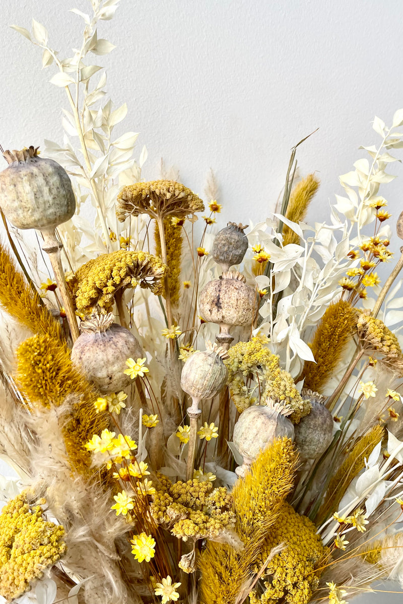 A dried floral arrangement with bright yellows and whites with hints of tan. 