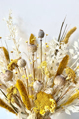 Dried floral in front of white wall. With the colors tan, white, and yellow.