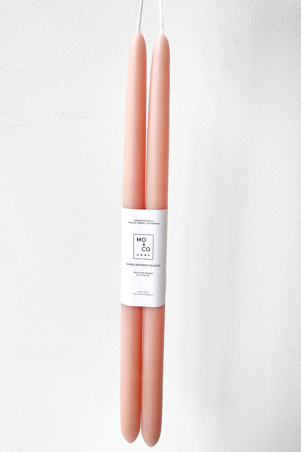 A hand holds Terra Cotta 14" Taper Candles, pair against a white backdrop