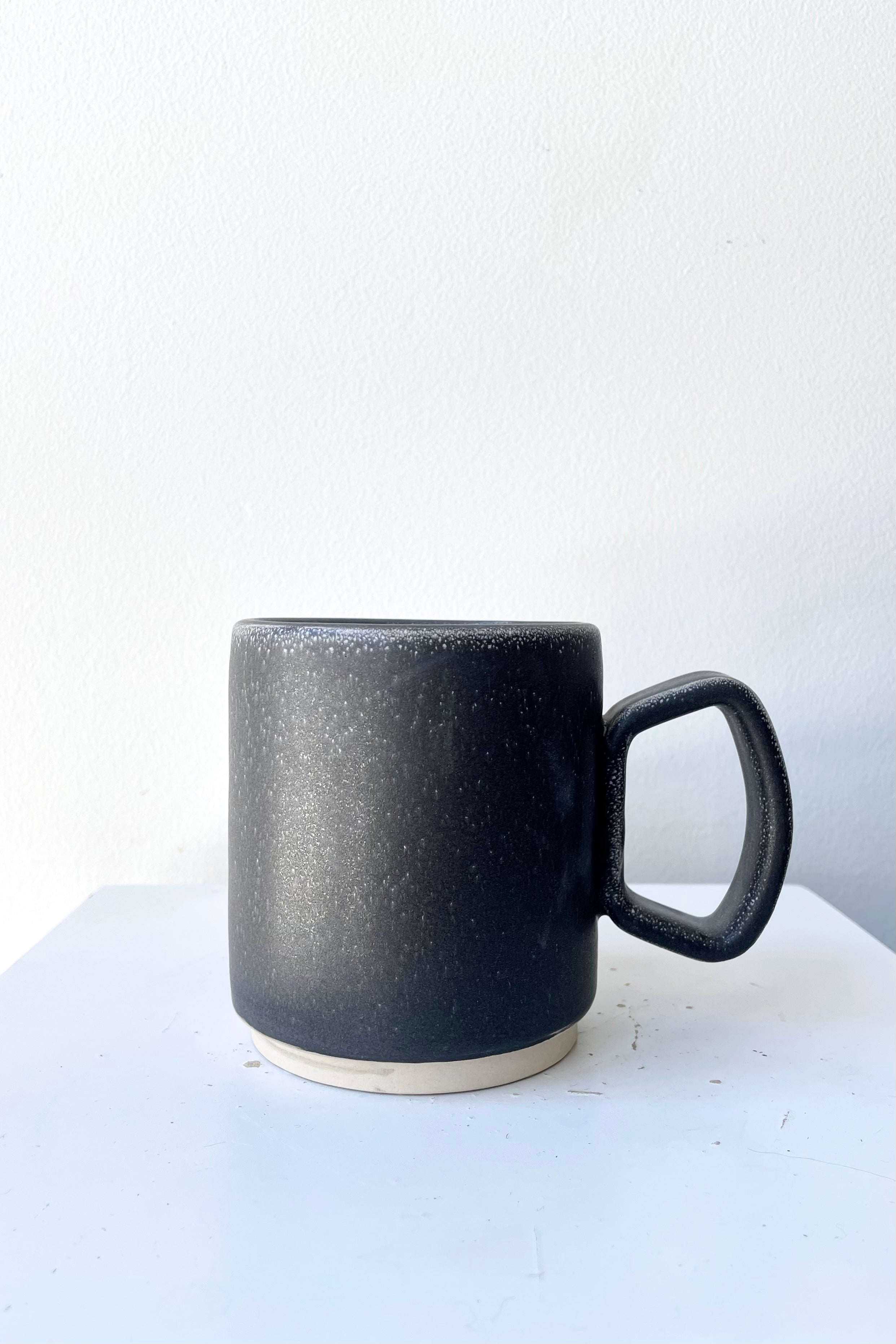 The grey black color of the ceramic Cosmos Tylor mug against a white wall at Sprout Home. 