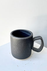 The grey black color of the ceramic Cosmos Tylor mug against a white wall at Sprout Home. 