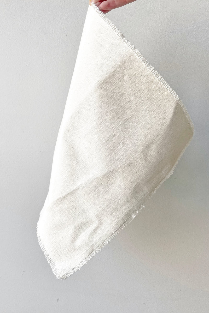 A hand holds the Raw Denim Napkin against a white backdrop