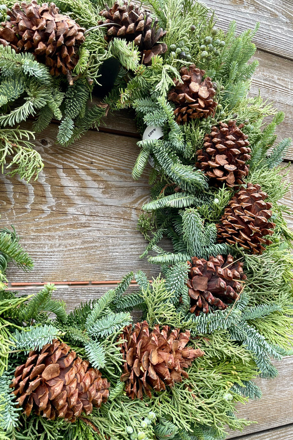 Holiday Pine cone wreath deluxe shown against a wood fence