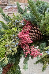 Evergreen wreath detail with pine cone and pepper berry.