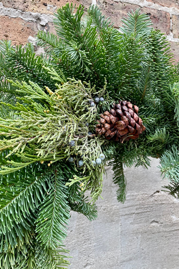 A detail picture of a mixed noble wreath showing the evergreen with a pine cone decoration.  