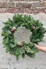 A 20" wised noble fir wreath against a concrete and brick wall. 