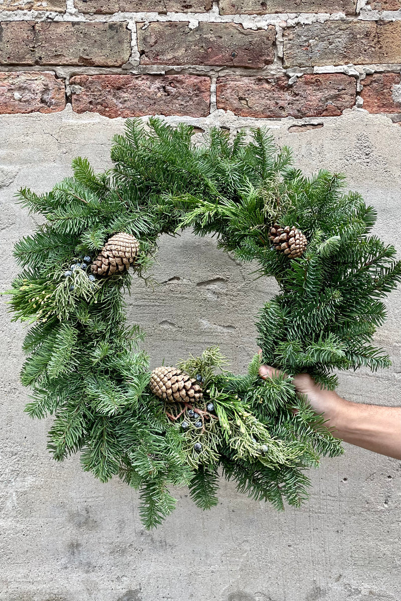 A 20" wised noble fir wreath against a concrete and brick wall. 
