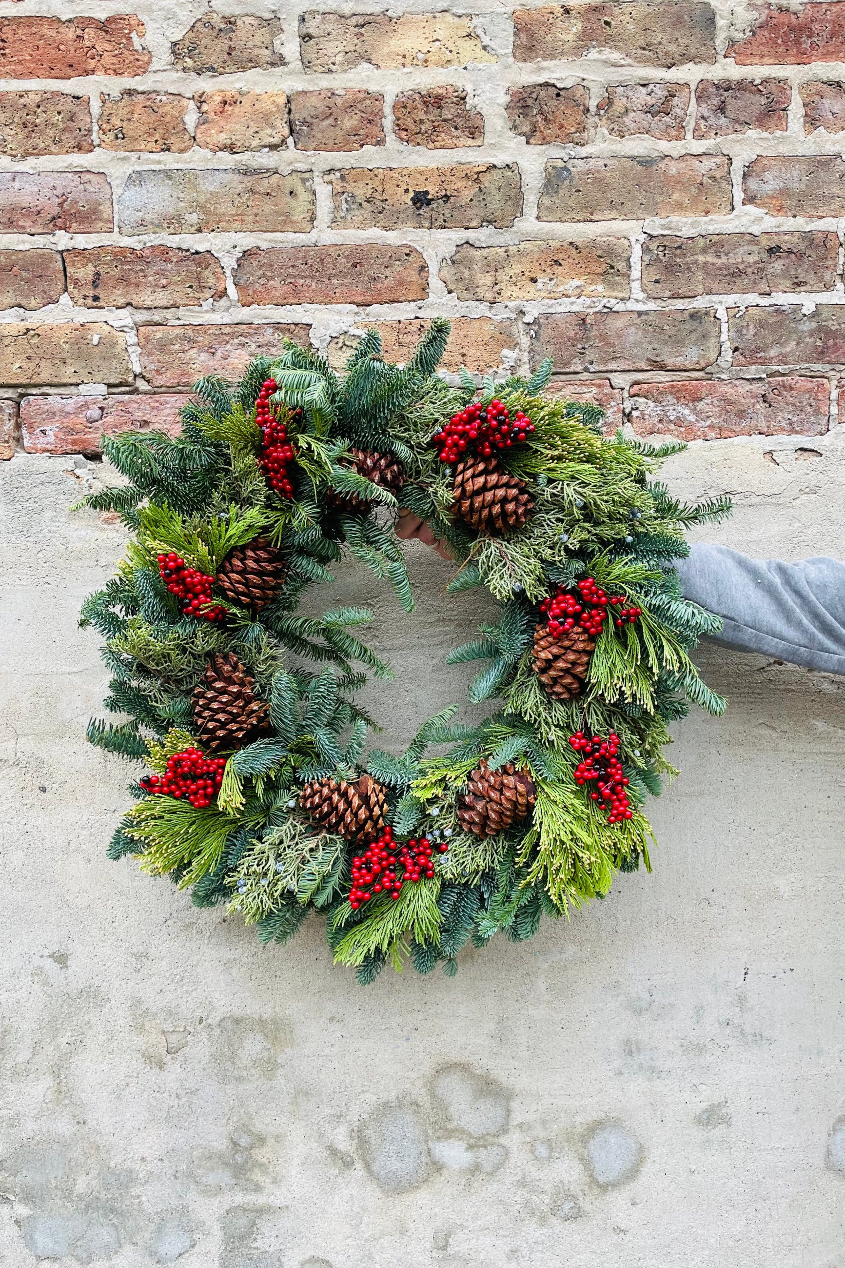 Multicone with faux canella berries evergreen wreath against a brick wall. ©Sprout Home