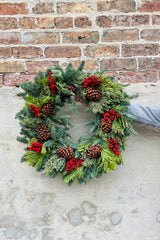 Multicone with faux canella berries evergreen wreath against a brick wall. 