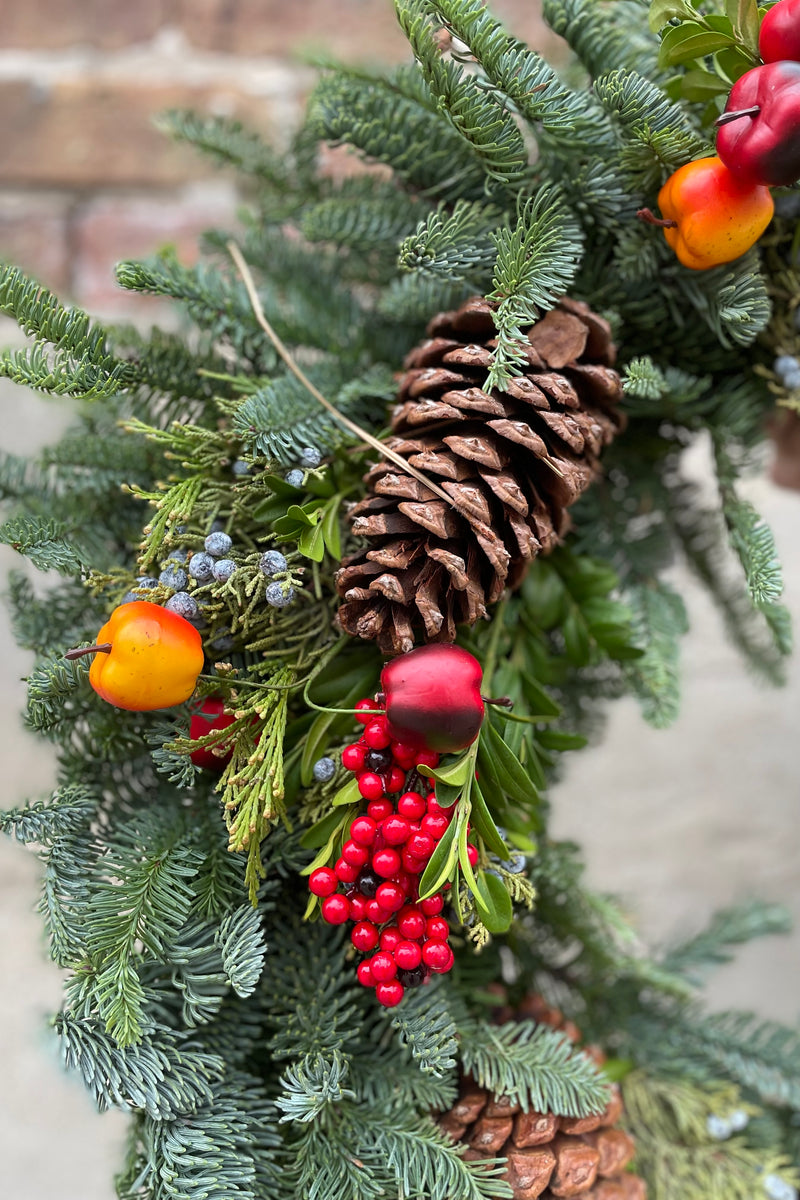 Detail shot of the faux fruit and pinecone on a royal fruit holiday wreath. 