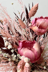 Chocoberry preserved floral arrangement by Sprout Home against a white wall showing details of the pink flowers and maroon leaves 