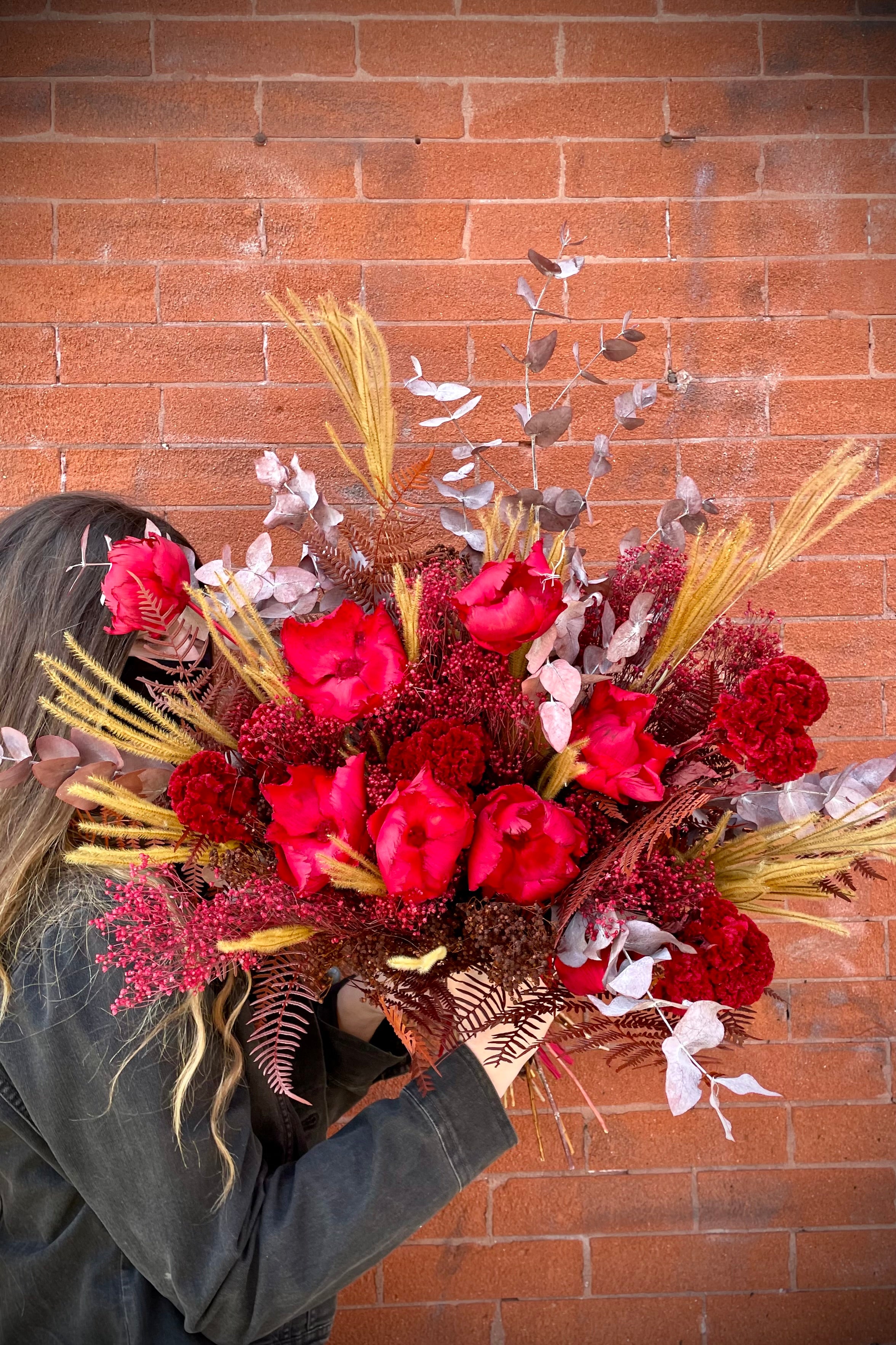Preserved Red Velvet arrangement against a red brick wall. #size_PLP