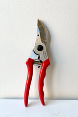 Red handled bypass pruners against a white wall