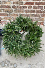 26" diameter Fraser fir wreath sigle sided being held against a concrete wall. 